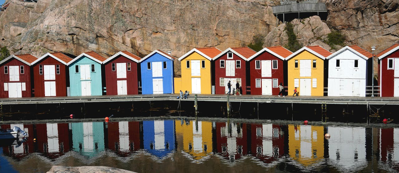 Färgglada sjöbodar speglas i vattnet i en svensk hamn