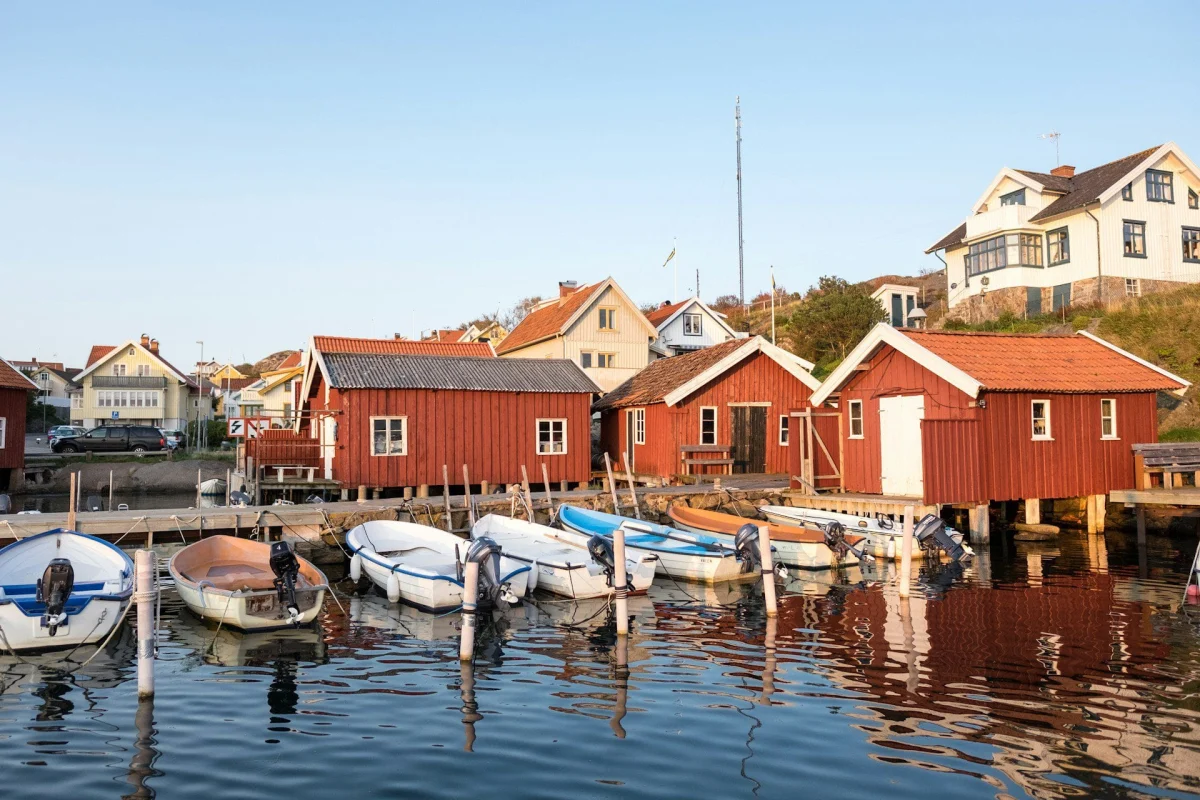 Båtar vid bryggan framför röda sjöbodar i en svensk hamn